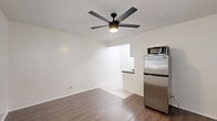 Located at 4451 Lockwood Ave in the heart of Los Angeles, CA, this efficiently designed studio offers a smart, single-floor layout that makes the most of every square foot. The combined kitchen and living area forms the heart of the space, featuring warm wood-look flooring, crisp white walls, and a modern ceiling fan with integrated lighting. The kitchen is outfitted with stainless steel appliances, including a compact refrigerator and microwave, complemented by dark countertops and a tile backsplash that adds a subtle decorative touch. A window with blinds allows natural light to filter into the living area, creating a bright and airy atmosphere. The bathroom is clean and functional, finished in white tile with a full bathtub and shower combo featuring chrome fixtures and overhead storage. The closet area is a standout feature, offering dual open closet spaces with built-in shelving and a louvered utility panel between them — maximizing storage in a compact footprint. High transom-style windows in the closet area bring in additional natural light. Throughout, the space maintains a cohesive, neutral palette that is both practical and easy to personalize.