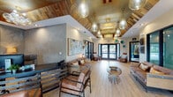 This single-floor space makes a striking first impression with its architectural centerpiece: a vaulted ceiling adorned with reclaimed wood planking and a metallic gold finish, from which an elegant cluster of glass teardrop pendant lights and a crystal chandelier descend to dramatic effect. Light hardwood flooring runs throughout, complementing the warm, industrial-chic aesthetic that defines the interior.

The main reception and lounge area is generously proportioned, featuring rich brown leather seating arranged around a sculptural sunburst accent table. Large floor-to-ceiling glass panels and black-framed double entry doors flood the space with natural light and provide views to the surrounding exterior. Abstract artwork and decorative wall pieces add curated personality to the neutral walls.

A dedicated office area is set apart, anchored by a bold industrial-style desk with a metal frame, flanked by leather seating and backed by large-format concrete-effect wall panels. Reclaimed wood cabinetry and soft accent lighting from table lamps create a refined yet approachable work environment beneath the same soaring vaulted ceiling.

Additional interior doors with louvered panels lead to ancillary rooms, while full-length glass partitions maintain visual openness throughout. The overall ambiance is sophisticated and inviting, blending rustic, industrial, and contemporary design elements seamlessly.