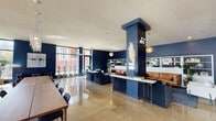 Located at 4736 N Winthrop Ave in Chicago's Uptown neighborhood, this single-floor space offers a thoughtfully designed communal lounge environment that balances modern aesthetics with functional versatility. The interior is defined by deep navy blue walls that create a rich, sophisticated backdrop throughout, contrasted by polished concrete floors that reflect natural light and add an industrial-modern character to the overall design.

Floor-to-ceiling windows along one side of the space flood the interior with abundant natural light while framing views of the surrounding streetscape and mature trees outside. The open layout is organized into several distinct zones without feeling compartmentalized. A long communal dining table with seating for numerous guests anchors one area beneath a cascading pendant light fixture, making it ideal for collaborative gatherings or shared meals.

A lounge area features a tan leather sofa positioned in front of white open shelving units styled with books, plants, and decorative objects against the navy walls. Warm pendant lighting in woven and globe styles adds an inviting ambiance. Structural columns with copper-accented console tables serve as elegant dividers within the open plan. Additional seating vignettes and potted greenery are distributed throughout, enhancing the welcoming and well-curated atmosphere of the space.