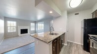 Located at 18050 Kelly Boulevard in Dallas, TX, this 1-bedroom, 2-bathroom residence offers a thoughtfully designed single-floor layout that maximizes functionality and comfort. The open-concept kitchen and dining area serve as the heart of the home, showcasing a peninsula with granite countertops, an undermount sink, dark cabinetry, and black appliances — all flowing seamlessly onto wood-style flooring. A pantry and adjacent hallway with built-in shelving provide generous storage. The living room features plush carpeting, a white brick fireplace, and a window that invites natural light, creating a warm and inviting atmosphere. The spacious bedroom is appointed with a ceiling fan, soft carpet, and a window with outdoor views, with direct access to a private bathroom featuring dark vanity cabinetry and granite countertops. A second full bathroom includes a tub-shower combo with tile surround and wood-style flooring. Additional highlights include a dedicated laundry area, a bonus room, multiple closets, and a connecting hallway that ties the layout together efficiently. Neutral tones and clean finishes throughout give the space a bright, move-in-ready feel.