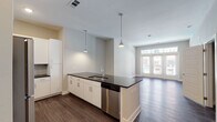 Located in Jacksonville, FL (32207), this single-floor residence offers a thoughtfully designed open-concept layout with consistent dark hardwood-style flooring throughout. The kitchen serves as a functional centerpiece, featuring white shaker cabinetry extending to the ceiling, dark granite countertops, a subway tile backsplash, and a full suite of stainless steel appliances including a refrigerator, range, microwave, and dishwasher. A peninsula island with pendant lighting provides additional counter space and separates the kitchen from the living area. The living room is bright and airy, anchored by a set of French doors with transom windows above that invite ample natural light and provide outdoor views. The bedroom is generously sized with a ceiling fan, a large window, and access to a spacious walk-in closet fitted with multi-level wire shelving for organized storage. The bathroom is well-appointed with a dual-sink vanity featuring granite countertops, white cabinetry, a large framed mirror, and a glass-enclosed shower. Neutral warm-gray walls, clean white trim, and recessed lighting lend a cohesive, modern aesthetic throughout the entire space.