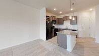 This single-floor residence in North Charleston, South Carolina offers a thoughtfully designed layout that balances comfort and modern style. The open-concept kitchen is a standout feature, showcasing rich dark cabinetry, a white subway tile backsplash, granite countertops, a kitchen island with pendant lighting, and black appliances including a refrigerator, range, microwave, and dishwasher. A built-in wine rack adds a refined touch to the culinary space. Light wood-style flooring runs through the kitchen and main living areas, creating a seamless, contemporary feel. The living space flows naturally from the kitchen, offering an inviting and functional layout. The bedrooms are generously proportioned, finished with plush neutral carpeting that adds warmth underfoot. Each bedroom benefits from natural light streaming through blinds-fitted windows, with ceiling fans providing year-round comfort. Views of the surrounding neighborhood are visible from the bedroom windows. The bathroom is well-appointed, featuring a dual-sink vanity with granite countertops, dark cabinetry with brushed nickel hardware, a large mirror, and wood-style flooring. A tub-shower combination completes the space. Neutral tones and clean lines throughout lend the residence a bright, move-in-ready ambiance.