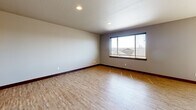 Located in Spokane, WA, this two-story home offers three bedrooms and three bathrooms thoughtfully distributed across two floors. The main level hosts the combined kitchen and living area, an attached garage with concrete flooring and interior access, and a hallway connecting key spaces. The kitchen is a standout, featuring rich dark-wood cabinetry, granite-style countertops, a classic subway tile backsplash, stainless steel appliances including a refrigerator, range, and built-in microwave, and light hardwood-style flooring that extends into the living area. A sliding door leads to a spacious outdoor deck complete with metal railings, outdoor seating, and open views of the surrounding neighborhood and landscape under wide Spokane skies. The upper floor houses the bedrooms, including a generously sized primary bedroom with its own walk-in closet outfitted with wire shelving and carpet flooring. Additional bedrooms feature carpet or hardwood-style floors and windows that bring in natural light. Bathrooms are finished with wood-toned vanities and vinyl plank flooring. A dedicated laundry room with full-size washer and dryer hookups and tile flooring adds everyday convenience. Rich wood baseboards and trim are consistent throughout, lending warmth and cohesion to the home's overall aesthetic.