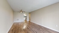 This single-floor residence offers a thoughtfully designed layout with a clean, neutral aesthetic throughout. The open living area is a standout feature, showcasing warm wood-look luxury vinyl flooring that reflects natural light, neutral beige walls, white baseboards, and a textured ceiling. A ceiling fan with a light fixture provides both airflow and ambient lighting. The living space connects seamlessly to the kitchen and a hallway leading to the bedrooms, creating an efficient and open flow.

A large sliding glass door in the living area floods the space with natural light and provides outdoor views, complementing the front entry door nearby. The kitchen is well-equipped with crisp white cabinetry, light-colored countertops, a soft blue subway tile backsplash, and a full suite of stainless steel appliances, including a range, microwave, dishwasher, and refrigerator. Wood-look flooring continues through the kitchen, maintaining design consistency.

The bedrooms are finished with plush neutral carpeting, ceiling fans, and ample wall space. One bedroom benefits from a window with outdoor views, allowing natural light to brighten the room. Both rooms offer access to adjoining spaces via interior doors, suggesting connected closet or bathroom access. Overall, the space presents a clean, move-in-ready environment with cohesive finishes throughout.