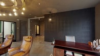 This single-floor commercial space presents a thoughtfully designed interior that blends industrial and contemporary aesthetics throughout. The reception and lounge area serves as the centerpiece, anchored by a dramatic circular tray ceiling adorned with a cascading arrangement of Edison bulb pendants on brass fittings, creating a warm, inviting ambiance. Large floor-to-ceiling windows and a glass-panel entrance door flood the space with natural light while offering open views of the surrounding streetscape.

A standout embossed tin-panel accent wall in deep charcoal adds bold texture and visual depth, complementing the polished concrete floors that run throughout. The lounge is furnished with rich cognac leather armchairs, a tufted green velvet sofa with accent pillows, wire bistro chairs, and a dark wood executive desk, creating a layered and eclectic feel. Textured herringbone wallcovering lines the interior corridors, lending warmth to the transitional spaces.

Beyond the lounge, a corridor leads to multiple private offices and meeting rooms accessed through both solid panel and glass-framed doors. The layout is efficient and purposeful, offering a variety of enclosed spaces suitable for focused work or private meetings. Overall, the space exudes a refined yet approachable character with careful attention to lighting, materials, and furnishings.