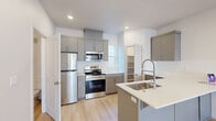 This three-story residence offers four bedrooms and four bathrooms distributed across thoughtfully arranged floors. The main level features a contemporary kitchen equipped with stainless steel appliances, including a refrigerator, range, and built-in microwave, complemented by grey shaker-style cabinetry, white subway tile backsplash, light wood-look flooring, and a peninsula with a deep stainless steel sink. A dedicated walk-in pantry with built-in shelving provides generous storage. The main floor also connects to a utility room and a bathroom, enhancing everyday convenience. The staircase, finished with carpet treads and clean white railings, links all three levels seamlessly. Bedrooms are carpeted and bright, receiving natural light through blinded windows, with the generously sized primary bedroom offering ample space. Each bathroom is finished with grey vanities topped with white countertops and brushed nickel or gold hardware; full bathrooms include a tub-shower combo with light wood-look tile flooring. The upper floor is the largest of the three, providing additional living space. Hallways on each level ensure smooth circulation throughout the home, and the clean, neutral palette of white walls and light finishes creates a bright, modern ambiance throughout.