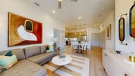 This thoughtfully designed one-bedroom, one-bathroom residence offers a modern open-concept layout that maximizes every square foot. Light wood-toned flooring flows throughout the main living areas, complementing the crisp white walls and elevated ceilings that lend an airy, spacious feel. The living room is a bright, welcoming space anchored by a ceiling fan and recessed lighting, with ample room for comfortable seating arrangements. It opens seamlessly to a well-appointed kitchen featuring flat-front wood cabinetry, a white quartz waterfall island with bar seating for three, stainless steel appliances, under-cabinet lighting, and pendant lights overhead — ideal for both everyday cooking and entertaining. The bedroom is a serene retreat with plush carpeting, large windows that invite natural light, and access to a closet. The full bathroom includes a tiled tub-shower combination, wood-accented cabinetry, and light wood flooring that ties the space together. Additional features include a dedicated hallway, a utility room, in-unit laundry, and a private patio. The overall ambiance is clean, contemporary, and functional, making this a well-rounded residence suited for modern living.
