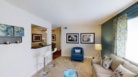 Located at 3105 Holston Ln in Raleigh, NC, this single-floor residence offers a thoughtfully designed layout that balances comfort and style. The living area serves as the heart of the home, featuring light-toned carpeting, crisp white walls, and a bold teal accent wall that adds a contemporary touch. Framed botanical artwork adorns the walls, contributing to a refined yet approachable aesthetic. A cozy seating arrangement, anchored by a blue accent chair and neutral sofa, creates an inviting atmosphere ideal for relaxing or entertaining. A pass-through counter with bar-height seating seamlessly connects the living area to the dining space, making the layout feel open and interactive. The dining area, visible through the pass-through, features warm hardwood-style flooring and a decorative chandelier overhead, offering a more intimate setting for meals. The warm, golden-toned walls in the dining area create a contrast with the lighter living space, adding visual depth throughout the home. The single-floor design ensures easy accessibility and a cohesive flow between living spaces, making this Raleigh residence a practical and stylish place to call home.