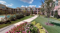 Located in Grand Prairie, Texas, this fitness center is part of a multi-story residential community featuring attractive stone and brick exterior architecture surrounded by lush, manicured landscaping, colorful flower beds, and a resort-style pool area. The fitness center itself is a thoughtfully designed, single-floor space finished with neutral tones, recessed lighting, and durable patterned carpet tile flooring throughout. The main workout area is lined with full-length mirrors that visually expand the space and enhance the exercise environment, and a wall-mounted flat-screen TV provides entertainment during workouts. Equipment includes strength-training machines, free weights, barbells, stability balls, and a hanging exercise mat, catering to a range of fitness routines. Ceiling fans provide additional air circulation across the space. A dedicated stretching and open-floor area offers room for yoga, mat work, or group exercise. Large floor-to-ceiling windows and glass doors along one wall frame sweeping views of the beautifully landscaped courtyard and pool area beyond, flooding the interior with natural light and creating a bright, inviting atmosphere. The seamless connection between the indoor fitness space and the outdoor amenity areas reflects a cohesive, community-focused design.