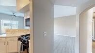 This single-floor residence offers a clean, modern aesthetic throughout, with light-toned luxury vinyl plank flooring that flows seamlessly across the main living areas and bedrooms. The open-concept layout connects the kitchen directly to the living space, creating a functional and cohesive floor plan. The kitchen is equipped with white cabinetry, a marble-style countertop, black appliances including a gas range with overhead microwave, a full-size refrigerator, and a dishwasher. A peninsula with a breakfast bar adds additional prep and seating space, while recessed lighting and an arched architectural detail add character to the room. The spacious living area is bathed in natural light from a large sliding glass door that opens to an outdoor area, with vertical blinds providing adjustable privacy. The bedrooms are generously sized with neutral-toned walls, and at least one features a walk-in closet with built-in rod and shelving. The bathrooms are well-finished, showcasing white vanity cabinetry, marble-style countertops, and large mirrors with bright overhead lighting. One bathroom features a double-sink vanity with a soaking tub. The overall ambiance is bright, clean, and move-in ready.