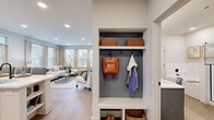 This thoughtfully designed one-bedroom, one-bathroom unit offers an efficient yet comfortable layout across its single-story floor plan. The open-concept kitchen and living area serves as the heart of the home, where the kitchen features white and gray shaker-style cabinetry, stainless steel appliances, a marble-style tile backsplash, and a peninsula with bar seating — ideal for casual dining. Light wood-tone flooring runs throughout the main living areas, complementing the neutral color palette. The living room benefits from multiple windows that invite abundant natural light and offer views of the surrounding neighborhood. A built-in mudroom alcove near the entry provides dedicated storage with upper shelving, wall hooks, and lower cubbies. The bedroom offers a cozy, carpeted retreat with a natural light-filled window and dedicated closet access. The bathroom is well-appointed with dual sinks set into gray shaker vanity cabinetry, a large framed mirror, and matte black hardware. A private balcony extends the living space outdoors, providing open views of the surrounding community.