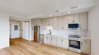 Located at 2126 North Lincoln Park West in Chicago's desirable Lincoln Park neighborhood, this one-bedroom, one-bathroom unit offers a thoughtfully designed layout with modern finishes throughout. Light hardwood flooring runs continuously across the entire space, contributing to a bright, cohesive aesthetic.

The kitchen is a standout feature, showcasing floor-to-ceiling soft-toned shaker cabinetry, a white subway tile backsplash, and stainless steel appliances including a refrigerator, range, and built-in microwave. A sleek black matte faucet and undermount sink add contemporary contrast, while a sliding barn door provides access to additional storage.

The open living area benefits from a large window offering views of the surrounding Lincoln Park cityscape, filling the space with natural light. The bedroom is comfortably sized with two windows that frame elevated neighborhood views, maintaining the unit's airy, light-filled character.

The bathroom is elegantly appointed with a geometric hexagonal tile floor, a walk-in glass-enclosed shower featuring black matte hardware and white textured tile walls, and a patterned shower floor for added visual interest.

A practical in-unit stacked washer and dryer is conveniently located off the bedroom hallway, adding everyday functionality to this well-appointed Chicago residence.