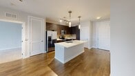 This third-floor unit at 5421 Lynx Ln in Columbia, MD offers a thoughtfully designed single-level layout with two bedrooms and two full bathrooms. The open-concept living and kitchen area serves as the heart of the unit, featuring rich hardwood-style flooring, track lighting, and a large center island with a white quartz countertop and undermount sink. Pendant lights hang above the island, complementing the dark espresso cabinetry, tile backsplash, and stainless steel appliances, including a French door refrigerator, range, and microwave. The living area receives natural light through a broad window with a ceiling fan overhead.

Both bedrooms are carpeted and finished with neutral tones, each providing direct access to a private bathroom and dedicated closet with built-in shelving. The primary bathroom features a glass-enclosed walk-in shower with floor-to-ceiling tile, while the secondary bathroom includes a soaking tub with similarly tiled surround. Dark wood vanities add contrast against the light tile flooring in both bathrooms. A louvered closet door near the kitchen provides additional storage. Overall, the unit presents a clean, modern aesthetic with consistent finishes throughout.