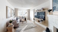Located at 5109 S Delaware St in Englewood, Colorado, this single-floor residence offers a thoughtfully designed layout with a warm, contemporary aesthetic throughout. The living room is a welcoming focal point, featuring light wood-style flooring, a textured ceiling, large windows that invite an abundance of natural light, and a built-in media wall with open shelving. The space is well-proportioned, comfortably accommodating a generous sectional seating arrangement centered around a round coffee table.

The kitchen is outfitted with white cabinetry, a decorative tile backsplash, stainless steel appliances including a refrigerator and microwave, and a peninsula that opens to the adjacent dining area. The dining space features a stylish chandelier and patterned accent wall, adding visual interest to everyday meals.

The bedroom is a serene retreat with plush carpeting, a sliding glass door offering outdoor access, and a trio of round mirrors above the bed that lend a modern touch. The full bathroom includes a soaking tub with shower and clean, neutral finishes. A dedicated laundry area with a full-size washer and dryer, topped by overhead cabinetry, adds everyday convenience to this well-rounded Englewood residence.
