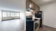 Located at 5277 W 82nd St in Bloomington, MN, this single-floor unit offers a practical and well-appointed layout designed for comfortable everyday living. The kitchen serves as a functional centerpiece, featuring a galley-style configuration with rich, dark-stained wood cabinetry extending to the ceiling for ample storage, white countertops, a subway tile backsplash, a stainless steel sink, and stainless steel appliances including an electric range and refrigerator. The kitchen opens directly toward the living area, creating a connected flow throughout the main space.

The living room is generously proportioned, bathed in natural light through a wide bank of windows that frame outdoor greenery. Hardwood-style flooring runs throughout the living and kitchen areas, lending a clean, modern aesthetic. A ceiling fan adds practical comfort to the living space.

The bedroom offers plush carpeting, a natural window view, and dual louvered closets providing substantial storage. A decorative chair rail adds a subtle architectural detail to the room.

The bathroom is finished with classic white mosaic tile flooring, white subway tile surround, a built-in tub and shower combination, and a white vanity with understated cabinetry, presenting a clean and timeless appearance throughout.