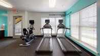Located at 650 Bentley Ridge Blvd in Lancaster, Pennsylvania, this well-equipped fitness center offers a comprehensive workout environment designed to support a wide range of exercise routines. The single-floor facility is thoughtfully laid out to maximize usable space while keeping the atmosphere open and energizing.

The interior features a bold teal and white color scheme, with motivational phrases displayed prominently on the walls — including "Push Yourself Beyond," "The Journey of a Thousand Miles Begins with a Single Step," and "Challenge, Believe, Change, Motivation, Success." These design elements contribute to an uplifting and goal-oriented ambiance throughout the space.

The cardio section is well-appointed with multiple treadmills, elliptical trainers, and stationary bikes, all positioned near large windows fitted with horizontal blinds that allow ample natural light into the room. The strength-training area includes cable machines, a multi-station weight system, a medicine ball rack, an adjustable workout bench, and a dumbbell rack. Full-length mirrors line portions of the walls, enhancing the sense of space and allowing for form checks during exercise.

Durable rubber flooring covers the entire facility, providing safety and comfort underfoot. Additional amenities include a water fountain, a wall-mounted split HVAC unit for climate control, and overhead fluorescent lighting. The space is clean, organized, and well-maintained throughout.