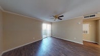 This single-floor unit offers a practical and well-appointed layout designed for comfortable living. The open living area is finished with dark hardwood-style flooring that extends throughout the main spaces, complemented by crisp white crown molding and clean white baseboards that add a polished touch. A ceiling fan with a light fixture serves both the living room and an adjoining area, providing airflow and ambient lighting. Vertical blinds cover a sliding glass door in the living room, which opens to an outdoor area and allows natural light to fill the space. A built-in HVAC vent is integrated into the wall, ensuring efficient climate control.

The galley-style kitchen features granite-look countertops, white cabinetry, a stainless steel sink, and white appliances including a refrigerator, electric range, and over-the-range microwave. The layout maximizes functionality within a compact footprint, with a pass-through counter connecting the kitchen to the living area.

The bedroom is carpeted in a warm brown tone, offering a softer underfoot feel, and receives natural light through a window. The bathroom includes a full tub-shower combination with white tile surround, paired with hardwood-style flooring for easy maintenance. The overall color palette of neutral beige tones creates a cohesive and understated ambiance throughout.