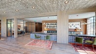 Located at 510 W Cabarrus St in downtown Raleigh, NC, this single-floor commercial space for Oldham & Worth masterfully blends historic industrial character with modern, refined design. The entrance is defined by dramatic floor-to-ceiling steel-framed glass doors and windows that flood the interior with natural light while offering clear views to the street. Exposed brick walls run throughout, providing warmth and texture that contrast beautifully with the ornate pressed tin ceilings overhead — a standout architectural feature that adds historic charm and visual depth to the entire space.

Wide-plank hardwood floors in a light, natural finish anchor the open layout and flow seamlessly between zones. A welcoming lounge area is furnished with a tufted velvet sofa, patterned area rugs, and accent chairs, creating an inviting and comfortable atmosphere. The reception and work area features built-in cabinetry with a sleek countertop workspace, task lighting, and a bold oversized Oldham & Worth logo display along the wall, reinforcing a strong brand identity. Glass-partitioned rooms provide private meeting or office areas while maintaining visual openness throughout. The overall ambiance is sophisticated yet approachable, balancing professional functionality with a warm, design-forward aesthetic.