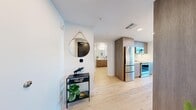 Located in Seattle's South Lake Union neighborhood, this one-bedroom, one-bathroom residence offers a thoughtfully designed layout with modern finishes throughout. Light hardwood flooring flows seamlessly across the entire space, complementing the clean white walls and exposed concrete ceilings that lend an urban, industrial character.

The living room is a standout feature, anchored by floor-to-ceiling windows that frame sweeping high-floor views of the Seattle skyline, Elliott Bay, and the surrounding cityscape, flooding the room with natural light. A dedicated dining nook adds functional versatility to the space.

The galley-style kitchen is efficiently appointed with warm wood cabinetry, white quartz countertops, a subway tile backsplash, and a full suite of stainless steel appliances including a refrigerator, range, oven, and built-in microwave.

The bedroom continues the modern aesthetic with exposed concrete ceiling details and a large window showcasing expansive city and water views. A dedicated closet provides ample storage.

The bathroom features wood-toned cabinetry, a white countertop vanity, and a walk-in shower. A stacked in-unit washer and dryer adds everyday convenience. The entry hallway is enhanced by a round decorative mirror, creating a welcoming arrival experience.