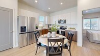 Located in South Jordan, Utah, this two-story home offers a thoughtfully designed layout across two floors. The entry level features a welcoming hallway with light wood-style flooring, clean white walls, and grey interior doors, setting a modern and cohesive tone throughout. An attached two-car garage with an automatic opener provides convenient access and additional storage space.

The open-concept kitchen and living area is a standout feature of the home. The kitchen is appointed with two-tone cabinetry — warm wood lower cabinets paired with crisp white uppers — complemented by white quartz countertops, stainless steel appliances, and a large single-basin sink beneath a window. The adjacent living area is bright and inviting, with large windows that bring in generous natural light and views of the surrounding neighborhood.

Upstairs, both bedrooms are carpeted and well-proportioned. The primary bedroom features recessed lighting, a large window, and ample closet space. The second bedroom includes a closet and direct access to a full bathroom. Both bathrooms echo the modern design language with wood-toned floating vanities, white countertops, light wood-style flooring, and windows that enhance ventilation and brightness. Three closets throughout the home ensure plentiful storage.