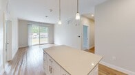 Located at 33 Highland Glen Dr in Randolph, MA, this well-appointed single-floor residence offers three bedrooms and three bathrooms in a thoughtfully designed layout. The modern kitchen is a standout feature, showcasing white shaker cabinetry, stainless steel appliances including a refrigerator, range, microwave, and dishwasher, and a large central island with pendant lighting overhead. Light hardwood flooring flows throughout the main living and kitchen areas, complemented by neutral-toned walls that lend a clean, contemporary feel. A sliding glass door connects the living area to a private outdoor deck, filling the space with natural light and providing easy outdoor access. The three bedrooms are finished with plush carpeting and feature generous closet space, including double-door closets in the primary bedroom. The primary bedroom is a comfortable size, offering a private and restful retreat. The three bathrooms are well-equipped, with one featuring a tiled tub-shower combination with classic subway tile, another offering a glass-enclosed shower stall, and a third with accessibility grab bars. Clean white cabinetry and light countertops are consistent across all bathrooms, reinforcing the home's cohesive, modern aesthetic.
