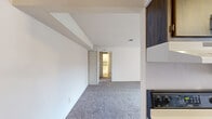 This single-floor, one-bedroom, one-bathroom unit offers a practical and straightforward layout across a modest but efficiently utilized footprint. The floor plan includes a living and dining area, a dedicated kitchen, a hallway, and one bedroom, providing a well-defined separation of spaces.

The living and dining area features neutral white walls and soft gray carpeting, creating a clean, understated backdrop. A structural beam detail adds a subtle architectural element to the ceiling. The space flows naturally toward the bedroom corridor, lending a sense of depth to the interior.

The galley-style kitchen is outfitted with dark wood cabinetry on both sides, offering ample storage. Light wood-tone flooring, a double stainless steel sink, a dishwasher, electric range, and a full-size refrigerator complete the functional workspace.

The bedroom is a well-proportioned room with warm-toned carpet, a window that allows natural light, and a built-in closet with bifold doors and upper shelving, providing practical storage.

The bathroom includes a vanity with a marble-patterned countertop, a toilet, and a shower-tub combination accented by a decorative diamond-patterned tile border in teal and tan. Wood-tone flooring ties the space together with a clean, neutral finish throughout.