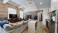 Located at 809 Chattanooga Ave in Dalton, GA, this 2-bedroom, 1-bathroom loft showcases a striking industrial aesthetic rooted in its building's historic character. The open-concept living and kitchen area is the heart of the space, featuring dramatic vaulted ceilings with exposed white-painted wooden beams, original exposed brick walls, and polished concrete floors that add raw, urban texture throughout. Pendant lighting drops from the ceiling, complementing the abundant natural light that streams through large arched windows.

The kitchen is outfitted with dark espresso cabinetry, stainless steel appliances including a refrigerator, range, microwave, and dishwasher, along with a central island that serves as both a prep and dining area. A pantry and dedicated laundry area provide added functionality.

The primary bedroom features soaring ceilings, an exposed brick accent wall, a large window, and a curtained closet, creating a cozy yet airy retreat. The second bedroom is finished with neutral tones, carpeted flooring, and a generous built-in closet. The bathroom is clean and simply appointed with a shower/tub combination. Additional storage is available via an included pantry and closet. This loft offers a compelling blend of historic industrial character and modern convenience.