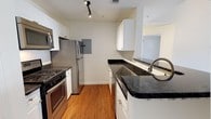 This two-floor, one-bedroom, one-bathroom residence delivers a thoughtfully designed layout across a comfortable footprint. The kitchen serves as a standout feature, showcasing dark granite countertops that contrast elegantly with crisp white cabinetry extending to the upper walls for generous storage capacity. A peninsula with a built-in sink and brushed nickel faucet provides additional prep space and casual dining potential. Stainless steel appliances, including a gas range, built-in microwave, dishwasher, and full-size refrigerator, complete the kitchen's functional and modern aesthetic. Track lighting mounted on the ceiling ensures well-distributed illumination throughout the cooking area. Warm-toned hardwood flooring runs throughout the kitchen, lending a cohesive and inviting feel to the space. Neutral wall tones throughout create a clean, versatile backdrop suitable for a variety of décor styles. The two-floor configuration offers a natural separation between living and private spaces, enhancing the overall sense of a home-like environment. This residence combines practical design with quality finishes, making it a well-rounded living option.