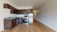 This single-floor unit presents a cohesive modern design highlighted by warm hardwood-style flooring that runs continuously throughout the living spaces. The kitchen serves as a functional centerpiece, outfitted with rich dark espresso cabinetry offering generous upper and lower storage, granite countertops with subtle speckled patterning, and a full suite of stainless steel appliances including a Samsung range with double oven, built-in microwave, refrigerator, and dishwasher. A undermount sink with a contemporary faucet completes the kitchen's practical layout.

The open living area adjoins the kitchen seamlessly, providing a flexible and generously proportioned space bathed in natural light. A sliding glass door offers direct access to an outdoor area while framing exterior views, contributing to an airy and open ambiance. The clean, neutral-toned walls throughout create a versatile backdrop adaptable to a variety of interior styles.

The bathroom continues the unit's consistent design language, featuring a dark vanity with granite countertop, an undermount sink, modern hardware, a large mirror, and hardwood-style flooring, all contributing to a polished and cohesive finish across the entire space.