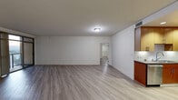 This single-floor unit offers a contemporary and functional layout designed with clean lines and modern finishes throughout. The open living and dining area is spacious and airy, featuring light-toned wood-look flooring, white walls, and flush ceiling lighting that creates a bright, welcoming atmosphere. A hallway connects the main living space to the additional rooms beyond.

The kitchen is a standout feature, showcasing rich warm-toned cabinetry on both upper and lower levels, dark countertops, a crisp white subway tile backsplash, a stainless steel gas range, and a sleek overhead range hood — combining style with practical functionality.

The bathroom is well-appointed with a warm wood vanity, an undermount sink with modern fixtures, large-format light tile flooring, and a full soaking tub with a glass sliding shower enclosure, all complemented by a large mirror and contemporary lighting.

The bedroom areas continue the wood-look flooring and neutral palette, with one room featuring floor-to-ceiling windows fitted with vertical blinds that open to a balcony offering sweeping views of the surrounding cityscape and distant hills, allowing abundant natural light to fill the space. The overall design is cohesive, clean, and move-in ready.