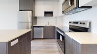Located at 202 Burnhamthorpe Rd E in Mississauga, this modern one-bedroom, one-bathroom condo offers a thoughtfully designed open-concept layout finished with light-toned hardwood flooring throughout. The combined kitchen and living area forms the heart of the unit, where a sleek kitchen impresses with two-toned cabinetry — dark wood lower cabinets paired with crisp white uppers — a white quartz countertop, subway tile backsplash, and a full suite of stainless steel appliances including a refrigerator, dishwasher, electric range, and built-in microwave. A central kitchen island provides additional prep and storage space. The bright living area is anchored by floor-to-ceiling windows and a sliding glass door that opens onto a private balcony, offering scenic views of lush greenery and the surrounding Mississauga skyline. The bedroom is a calm, well-proportioned retreat featuring its own large window with balcony access, light-filled interiors, and a spacious sliding-door closet. A stacked in-suite washer and dryer is conveniently tucked nearby. The bathroom is finished with large-format marble-style porcelain tiles, a soaker tub with tiled surround, a white vanity, and a mirror. The unit also includes two hallway areas for smooth circulation throughout.