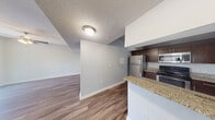 This two-story residence offers a well-organized layout across two floors, with the majority of the living space situated on the main level. The open-concept main floor integrates the living room and kitchen seamlessly, creating a functional and connected environment. The kitchen is equipped with dark espresso cabinetry, granite countertops, stainless steel appliances including a refrigerator, range, and microwave, and a breakfast bar that provides additional counter space and casual seating. Wood-style flooring runs throughout the main living areas, complementing the neutral gray walls and textured ceilings. The living room is bright and airy, featuring a ceiling fan and sliding glass doors that open to a balcony, allowing natural light and outdoor views. A dedicated laundry room on the main floor houses a full-size washer and dryer. The upper floor accommodates both bedrooms, each carpeted and fitted with ceiling fans. The generously sized primary bedroom includes a walk-in closet with wire shelving systems. The bathrooms feature tile flooring, tub-shower combinations with full tile surrounds, granite vanity countertops, and dark wood cabinetry, maintaining a consistent and cohesive finish throughout the home.