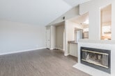 This single-floor residence offers a thoughtfully designed open-concept layout with a warm, neutral color palette and wood-look flooring that flows consistently throughout. The spacious living area is anchored by a classic tile-surround fireplace with a gold-trimmed insert, adding both character and comfort. Vaulted ceilings in select areas enhance the sense of openness, while a ceiling fan provides practical functionality. A pass-through counter connects the living space to the kitchen, creating an inclusive, connected feel.

The kitchen is well-equipped, featuring white shaker-style cabinetry, dark countertops, a stainless steel gas range, and a range hood. Natural light streams in through a window near the exterior door, brightening the space. A washer unit is also conveniently located within the kitchen area.

The bathroom is clean and modern, showcasing white cabinetry with brushed nickel hardware, a wide dark-toned countertop, an undermount sink, and a large wall mirror illuminated by a contemporary light bar. The bedroom features vaulted ceilings and a window that allows natural light to fill the room, contributing to an airy, restful atmosphere. Overall, the space presents a cohesive, move-in-ready environment with practical features and contemporary finishes.