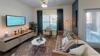 This single-story residence at 6310 S State Hwy 360 offers a well-designed layout that balances functionality with contemporary style. The living area serves as the heart of the space, featuring wood-look flooring, a ceiling fan with light fixture, and a large window dressed with deep green curtains that invite natural light while providing privacy. The dining area sits adjacent to a glass-paneled exterior door, brightened by additional windows that frame outdoor views.

The kitchen is outfitted with rich dark cabinetry, granite-style countertops, and black appliances including a range and over-the-range microwave. Wood-look flooring continues through this space, adding warmth and cohesion.

The bedrooms offer distinct character. The primary bedroom features a dramatic dark accent wall, warm Edison-style sconce lighting, and access to a walk-in closet. The second bedroom is bright and airy, with large windows, light carpet, and barn-style curtain hardware.

The bathroom is well-appointed with an extended dark wood vanity, a wide mirror, light countertops, wood-look flooring, and a tub-shower combination. The overall ambiance throughout the unit is modern and inviting, with consistent dark wood tones anchoring each space.
