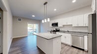 Located at 1055 Bridgeport Avenue in Shelton, CT, this well-appointed one-bedroom, one-bathroom residence offers a thoughtfully designed layout with modern finishes throughout. The open-concept kitchen and living area serves as the heart of the home, showcasing white shaker cabinetry, granite countertops, a central island with pendant lighting, and a full suite of stainless steel appliances including a range, microwave, dishwasher, and refrigerator. Wood-style flooring runs throughout, adding warmth and continuity to the space. Sliding glass doors lead to a private balcony, allowing natural light to flood the living area and offering pleasant outdoor views. The spacious primary bedroom features neutral tones, wood-style flooring, a large window overlooking the outdoors, and access to two closets, providing ample storage. The bathroom is finished with a sliding-glass walk-in shower, granite-topped vanity, and coordinating wood-style flooring. Additional conveniences include a dedicated laundry area and a hallway that connects the living spaces efficiently. Clean lines, recessed lighting, and a neutral color palette give this residence a fresh, contemporary feel throughout.