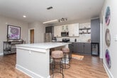This single-floor, two-bedroom residence offers a thoughtfully designed layout that balances functionality and contemporary style. The open-concept kitchen serves as a central highlight, featuring a large island with quartz countertops and a double basin sink, stainless steel appliances, a subway tile backsplash, and a striking two-tone cabinet design pairing crisp white uppers with dark wood-grain lowers. Track and pendant lighting enhance the workspace, while an in-unit washer and dryer area is conveniently tucked nearby.

The living area provides a welcoming atmosphere with warm, wood-look flooring, a ceiling fan, and natural light streaming through multiple windows with blinds and drape treatments. A private entry door adds accessibility and convenience.

The primary bedroom is generously sized with plush carpet, a ceiling fan, a walk-in closet, and a dedicated en-suite bathroom featuring a soaking tub with subway tile surround. The second bedroom also offers carpeted flooring, a ceiling fan, and natural light. A second bathroom serves this room, complete with a glass-enclosed walk-in shower, a dark-framed vanity mirror, and quartz countertops. Neutral gray tones and wood-look flooring carry throughout the bathrooms, tying the home's design together cohesively.