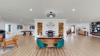 Located at 501 SW 20th St in Bentonville, Arkansas, the Touchstone Village community clubhouse is a thoughtfully designed single-story facility that serves as a central hub for residents. The space is anchored by a striking reception area, where a distinctive front desk — accented with stacked firewood displays and a built-in fireplace — sets a warm yet contemporary tone. The Touchstone Village logo is prominently displayed on the feature wall, giving the entrance a polished, branded identity. Light hardwood-style flooring flows seamlessly throughout, unifying the various zones of the facility.

The expansive lounge area offers generous seating with plush white sofas, mid-century modern accent chairs, and a large round wood coffee table, all complemented by curated artwork and natural light streaming in through multiple windows. A wall-mounted television and fireplace make this an inviting space for relaxation and socializing. Adjacent to the lounge, a game room with a full-size pool table provides recreational options for residents.

A utility and resource area features bold navy built-in shelving for organized storage, alongside access to a refreshment station. A private office with a dedicated desk and seating offers a quiet space for consultations or administrative needs. A bright dining nook, illuminated by a statement pendant light and surrounded by windows, provides an intimate setting for casual gatherings. Together, these spaces create a vibrant, functional, and aesthetically cohesive community environment.