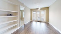This single-floor residence offers a thoughtfully designed layout with a clean, contemporary aesthetic carried consistently throughout each room. The kitchen serves as a functional centerpiece, showcasing rich dark wood cabinetry extending to the ceiling, stainless steel appliances including a French door refrigerator, electric range, and built-in microwave, complemented by light quartz countertops and a subway tile backsplash. A large island with a double stainless steel sink and elegant pendant lighting adds both style and practicality. Warm hardwood-style flooring runs through the main living and kitchen areas, while the living room benefits from natural light through French doors and features a ceiling fan and built-in shelving. An adjacent carpeted bedroom continues the neutral palette, with blinds covering windows and its own ceiling fan for comfort. Both bathrooms are finished with light tile flooring, modern dark vanity cabinetry, white quartz countertops, and framed mirrors. One bathroom provides convenient access to a dedicated walk-in closet fitted with a hanging rod and shelving. The overall ambiance is modern and inviting, with warm beige wall tones, white trim, and consistent finishes creating a cohesive and comfortable living environment.