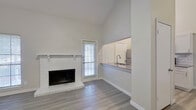 This two-story home offers a thoughtfully designed layout with modern updates and clean finishes throughout. The main living area commands attention with soaring vaulted ceilings and a classic white-painted brick fireplace, creating a warm yet airy atmosphere. Natural light filters in through multiple windows, enhancing the light gray luxury vinyl plank flooring that runs consistently across both levels.

The galley-style kitchen is well-appointed with white cabinetry, subway tile backsplash, gray quartz countertops, and a full suite of stainless steel appliances including a refrigerator, range, microwave, and dishwasher. A pass-through counter connects the kitchen to the living area, promoting an open flow between spaces.

A striking open staircase with white railings leads to the upper level, where multiple generously sized bedrooms are found, each featuring ceiling fans, ample natural light, and access to walk-in closets. The bathrooms are clean and functional, offering tub-shower combinations and built-in shelving in the closets.

Throughout the home, the neutral color palette, consistent flooring, and white trim create a cohesive, move-in-ready aesthetic that is both practical and inviting.