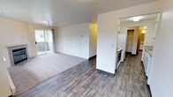 Located at 804 100th Ct E in Tacoma, Washington, this single-floor residence offers a clean and functional layout designed for comfortable everyday living. The open living area is a welcoming space featuring plush carpeting and an abundance of natural light streaming in through a large sliding glass door that leads to a private balcony, offering a pleasant outdoor connection. The transition from the carpeted living area to the hardwood-style flooring marks the entry into the kitchen and adjoining spaces, creating a clear and practical separation of zones. The kitchen is equipped with white appliances, including a refrigerator and a stove, and features ample cabinetry for storage. A dedicated pantry or closet area adjacent to the kitchen provides additional organizational space. The walls are finished in a neutral white palette throughout, complementing the natural tones of the flooring and creating a bright, airy atmosphere. The textured ceiling adds a subtle architectural detail. Overall, the space presents a straightforward and well-maintained interior that balances open living with practical functionality, making it a comfortable and efficient place to call home in the Tacoma area.