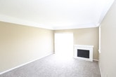 This single-floor residence offers a thoughtfully arranged layout with comfortable living spaces throughout. The main living area is generously sized, featuring plush wall-to-wall carpeting, warm neutral-toned walls, and a classic white-trimmed fireplace as a focal point. A large sliding glass door fitted with vertical blinds invites abundant natural light and provides access to the outdoors. Adjacent to the living area is a secondary carpeted room, also bathed in natural light through a large window and outfitted with a ceiling fan — ideal as a dining space or den. The bedrooms continue the warm, carpeted aesthetic, each equipped with ceiling fans for comfort. One bedroom features a walk-in closet, offering notable storage capacity. The U-shaped kitchen is efficiently designed with white cabinetry, light countertops, a gas range, dishwasher, and refrigerator, all complemented by a window above the sink that brings in natural light. The bathroom is clean and functional, featuring wood-look flooring, a shower-tub combo, a toilet, and a vanity with a speckled granite-style countertop and ample cabinet storage below. Throughout the space, a cohesive palette of neutral tones and white trim creates a bright, move-in-ready atmosphere.