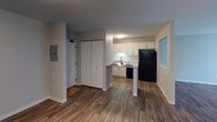 This single-floor 1-bedroom, 1-bathroom residence offers a clean, functional layout designed for comfortable everyday living. The entryway opens into a combined living and dining area finished with rich wood-look flooring that extends throughout the unit, creating a cohesive and warm aesthetic. A large sliding glass door floods the living room with natural light and provides direct access to an outdoor balcony area with greenery views, making the space feel open and inviting. A textured ceiling adds subtle character overhead, while a baseboard heating system ensures year-round comfort.

The kitchen is efficiently designed with white shaker-style cabinetry, light granite-pattern countertops, and a classic subway tile backsplash. Black appliances — including an electric range with overhead ventilation, a refrigerator, and a dishwasher — provide a bold contrast against the lighter cabinetry. A stainless steel double-basin sink with a modern pull-down faucet adds a practical finishing touch. A closet adjacent to the entry provides convenient storage, along with a visible electrical panel.

The bathroom features wood-look flooring, a full tub-and-shower combination with white tile surround, chrome fixtures, and an accessibility grab bar. A vanity with white cabinetry completes the space, offering ample storage and a tidy, functional finish.
