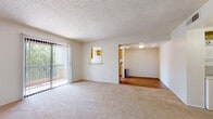 This single-floor residential unit offers a practical and comfortable layout across several well-defined living spaces. The living room is generously sized, featuring neutral wall-to-wall carpeting, a textured ceiling, and a large sliding glass door fitted with vertical blinds that opens to a private balcony, allowing natural light to fill the room and providing pleasant outdoor views of surrounding greenery. A pass-through window connects the living area to the kitchen, enhancing the open feel of the space.

The galley-style kitchen features warm oak cabinetry lining both walls, light wood flooring, a double-basin sink with a countertop workspace, and white appliances including a coil-top range and a full-size refrigerator. A narrow window at the end of the kitchen brings in natural light.

The unit includes two carpeted bedrooms, each with large windows framing leafy outdoor views and offering ample wall space for furnishing flexibility. One bedroom provides direct access to a hallway leading to additional areas of the unit.

Two bathrooms serve the unit, each featuring warm oak vanity cabinetry, light countertops, a large mirror with overhead lighting, and wood-look flooring. One bathroom includes a bathtub. The overall ambiance of the unit is clean, bright, and functional.