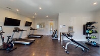 This fitness center in Kingsland, Georgia offers a comprehensive workout environment designed for convenience and functionality. The space is finished with durable diamond-plate rubber flooring throughout, providing excellent traction and cushioning for a wide range of exercises. Recessed lighting illuminates the room evenly, and neutral-toned walls create a clean, focused atmosphere.

The facility is well-stocked with cardio equipment, including multiple treadmills, an elliptical trainer, and a stationary spin bike. Strength training is supported by a multi-function cable machine, a flat weight bench, an adjustable incline bench, and a full rack of dumbbells in varying weights. Foam rollers and kettlebells are also available for warm-up and functional training. Wall-mounted flat-screen televisions are positioned throughout the room for entertainment during workouts.

Two sets of French doors line one wall, flooding the space with natural light and offering views of the outdoor pool area beyond, creating a bright and inviting atmosphere. A built-in water station provides easy hydration access. A mirrored panel and posted guidelines are also present for user convenience. The single-story layout ensures straightforward accessibility, making this fitness center a practical and fully outfitted amenity.
