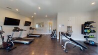 This fitness center in Kingsland, Georgia offers a comprehensive workout environment designed for convenience and functionality. The space is finished with durable diamond-plate rubber flooring throughout, providing excellent traction and cushioning for a wide range of exercises. Recessed lighting illuminates the room evenly, and neutral-toned walls create a clean, focused atmosphere.

The facility is well-stocked with cardio equipment, including multiple treadmills, an elliptical trainer, and a stationary spin bike. Strength training is supported by a multi-function cable machine, a flat weight bench, an adjustable incline bench, and a full rack of dumbbells in varying weights. Foam rollers and kettlebells are also available for warm-up and functional training. Wall-mounted flat-screen televisions are positioned throughout the room for entertainment during workouts.

Two sets of French doors line one wall, flooding the space with natural light and offering views of the outdoor pool area beyond, creating a bright and inviting atmosphere. A built-in water station provides easy hydration access. A mirrored panel and posted guidelines are also present for user convenience. The single-story layout ensures straightforward accessibility, making this fitness center a practical and fully outfitted amenity.