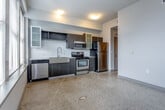 Located in the heart of Kansas City, Missouri, this single-floor urban residence at 300 E 12th St offers a thoughtfully designed layout with contemporary finishes throughout. The open living and kitchen area is a standout, featuring polished terrazzo flooring that adds a distinctive, timeless character to the space. A generous bank of large windows floods the room with natural light while framing impressive elevated views of the Kansas City skyline — a compelling focal point of the unit.

The kitchen is outfitted with a full suite of stainless steel appliances, including a refrigerator, electric range, built-in microwave, and dishwasher. Dark espresso cabinetry, a white subway tile backsplash, and a stainless steel sink complete the modern, functional aesthetic. The open layout allows the kitchen to flow seamlessly into the main living area, making the space feel connected and versatile.

The bedroom features soft carpeting, neutral tones, and a clean, understated design with practical closet access. The bathroom is finished with large-format gray tile in the shower/tub surround, a floating white vanity, terrazzo flooring, and an accent teal wall, lending a modern yet warm character. The overall ambiance is contemporary urban, well-suited for those looking to be immersed in the energy of downtown Kansas City.