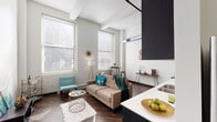 This single-floor loft-style unit showcases an industrial-modern aesthetic defined by dramatically high ceilings with exposed structural beams and visible ductwork, creating an airy, open ambiance throughout. Rich, dark hardwood flooring runs continuously across the main living areas, anchoring the space with warmth and contrast.

The open-concept living area is generously proportioned, featuring tall windows that flood the space with natural light. The kitchen is well-appointed with dark espresso cabinetry extending to ceiling height, white quartz countertops, stainless steel appliances including a range with hood vent, dishwasher, and refrigerator, along with a stacked in-unit washer and dryer located down a connecting hallway.

The bedroom offers an intimate atmosphere with soaring ceilings continuing from the main space. A unique dual-closet configuration with dark-framed doors provides ample organized storage. The bathroom is clean and functional, featuring a dark vanity with white countertop, a large mirror, and a tub-shower combination. Throughout the unit, the interplay of white walls, dark finishes, and industrial ceiling details creates a cohesive and contemporary loft character.
