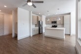 This single-floor residence showcases a clean, modern design defined by an open-concept layout that seamlessly connects the kitchen and living areas. Warm hardwood-style flooring runs throughout the main living spaces, complemented by crisp white walls and generous natural light streaming through multiple large, blinds-fitted windows. Ceiling fans are present in both the living area and bedroom, enhancing comfort year-round.

The kitchen is a standout feature, equipped with a full suite of stainless steel appliances, including a refrigerator with ice maker, electric range, microwave, and dishwasher. Soft gray cabinetry pairs with a white quartz countertop, while a subway tile backsplash adds textural interest. A central island with an undermount sink and pendant lighting overhead makes the space ideal for both cooking and casual dining.

The bedroom offers plush carpet flooring, a ceiling fan, and a walk-in closet with built-in shelving. The primary bathroom features a dual-sink vanity with quartz countertops, a framed mirror, and a glass-enclosed shower. A secondary bathroom provides a tub-shower combination, single-sink vanity, and mirrored storage cabinet, maintaining the space's consistent, polished aesthetic.
