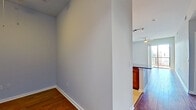 This single-floor, one-bedroom residence offers a thoughtfully designed layout that makes efficient use of its space. The open-concept kitchen and living area serves as the heart of the unit, featuring rich hardwood flooring, soaring ceilings, and a ceiling fan for added comfort. The kitchen is equipped with stainless steel appliances, including a French-door refrigerator, a microwave, and a range, complemented by warm wood cabinetry that extends to the ceiling for ample storage. A peninsula with a dark granite countertop and an undermount sink doubles as a breakfast bar, with pendant lighting overhead. Track lighting provides additional illumination throughout the space. The living area benefits from a wall of floor-to-ceiling sliding glass doors opening onto a private balcony with open neighborhood views. The bedroom is carpeted, features a ceiling fan, a large window with natural light, and connects to a dedicated closet with a hanging rod. The full bathroom includes a soaking tub with tiled surround, a dark-vanity with an integrated sink, and light tile flooring. A hallway connects all areas of the unit, providing a practical and organized flow throughout.