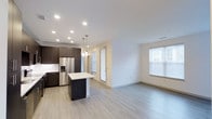 Located at 6963 E 109th Ave in Westminster, Colorado, this single-floor residence offers a thoughtfully designed open-concept layout that seamlessly connects the kitchen and living areas. The kitchen is a standout feature, showcasing dark espresso cabinetry that contrasts elegantly with a white countertop island, which serves as both a workspace and a casual gathering spot. Stainless steel appliances, including a French door refrigerator with an in-door ice and water dispenser, add a polished, contemporary feel. Pendant lighting hangs above the island, complementing the recessed ceiling lights that illuminate the space throughout. The light-toned laminate flooring extends across the entire open area, contributing to a clean, cohesive aesthetic. The living area is generously proportioned, with neutral walls that provide a versatile backdrop for any décor style. Large windows fitted with white blinds allow natural light to filter in, brightening the interior throughout the day. A glass-paneled door provides additional access and light. Overall, the space maintains a modern, minimalist ambiance with functional design elements.